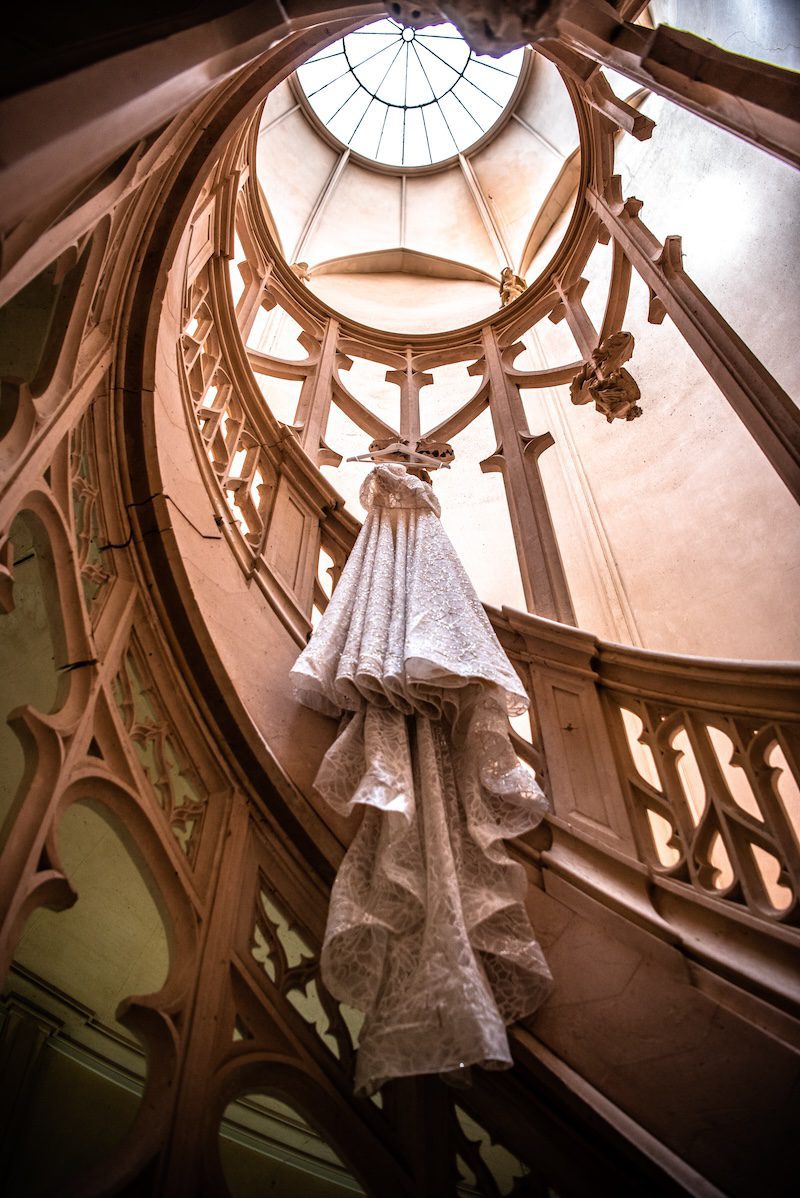a wedding dress hanging in the stairwell of an french castle